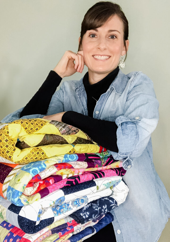 woman in jean jacket holding four patchwork quilts